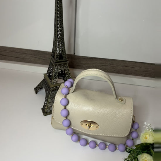 Mini-Parisienne borsa beige compatta con collana di perle viola coordinata, accanto a Torre Eiffel decorativa e fiori gialli