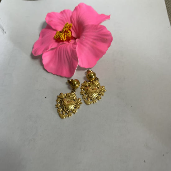 Orecchini dorati a forma di sacro cuore con dettagli intarsiati e lavorazione artigianale su sfondo con fiore rosa