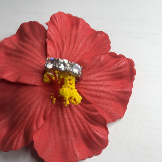 Anello Trio in acciaio premium placcato argento con tre zirconi brillanti perfettamente incastonati, fotografato su fiore rosso
