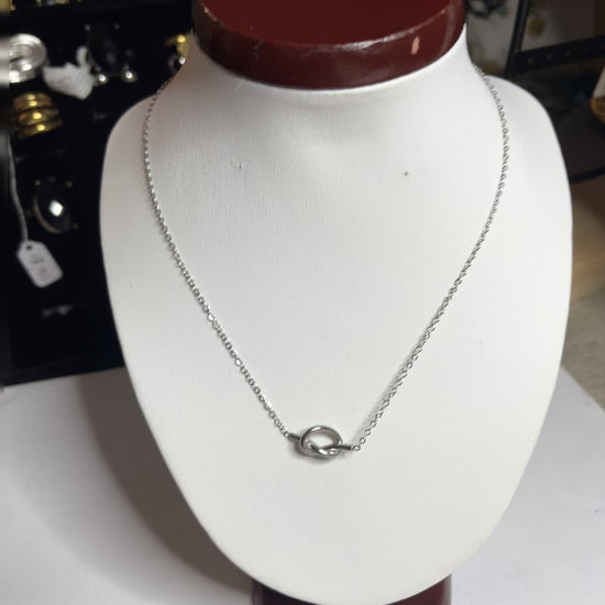 Collana Love Knot con pendente a nodo intrecciato dorato su catena delicata, simbolo di amore eterno esposto su busto bianco