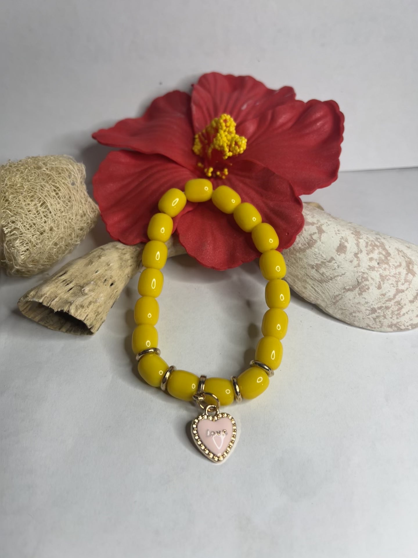 Braccialetto elastico con perle gialle dorate e ciondolo a cuore rosa su sfondo neutro
