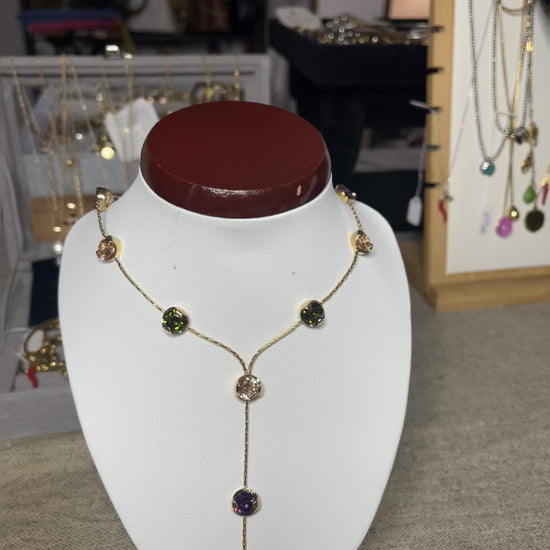 Collana Ottone e Cristalli Bohémien esposta su busto bianco, design asimmetrico con pendente lungo, cristalli verdi e viola incastonati in ottone dorato, stile bohémien elegante