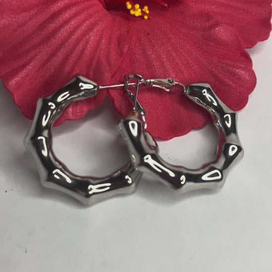 Orecchini Bambù Prezioso placcati argento con texture bambù a cerchio, design naturale elegante su sfondo bianco con fiore rosso decorativo