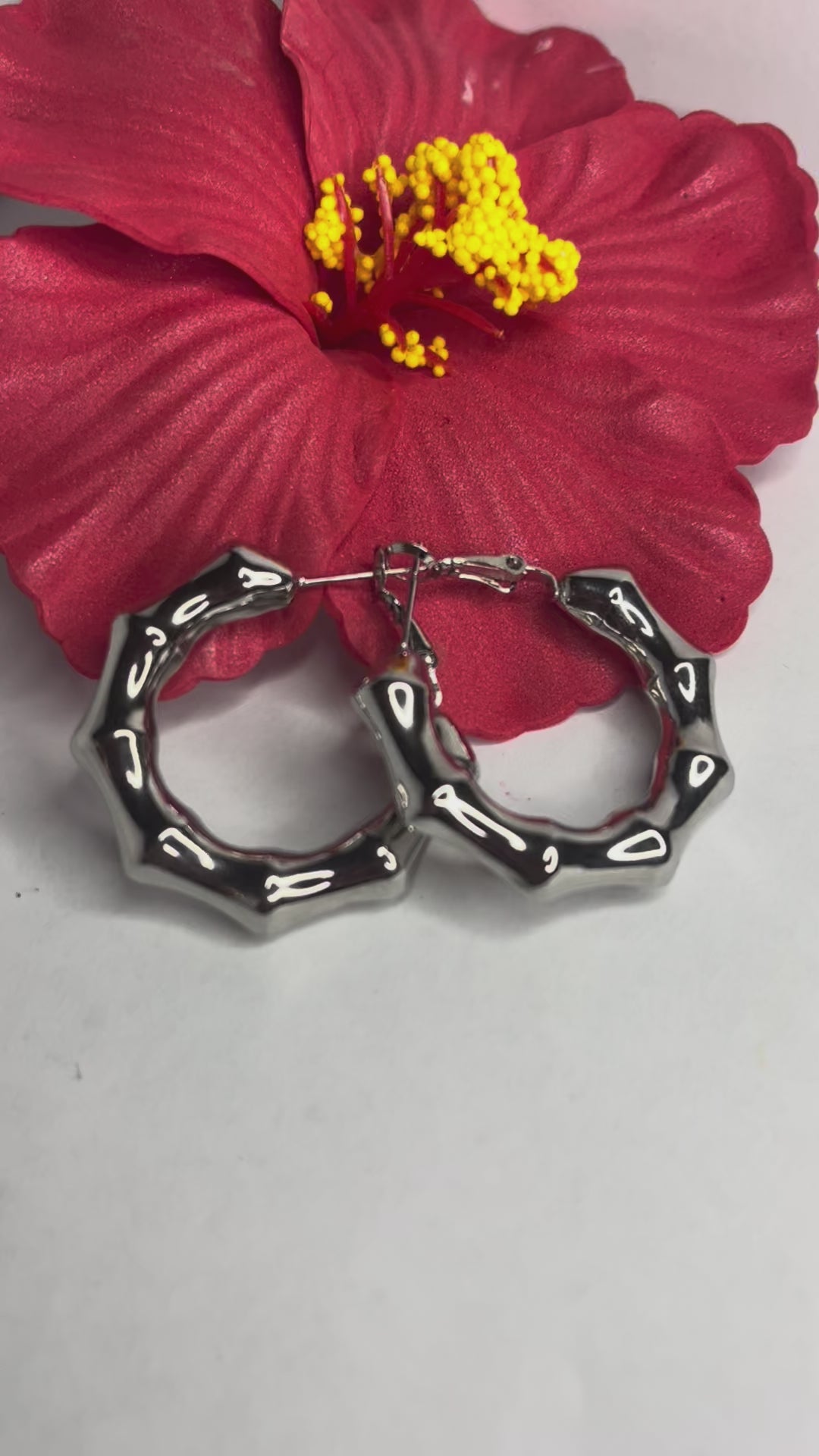 Orecchini Bambù Prezioso placcati argento con texture bambù a cerchio, design naturale elegante su sfondo bianco con fiore rosso decorativo