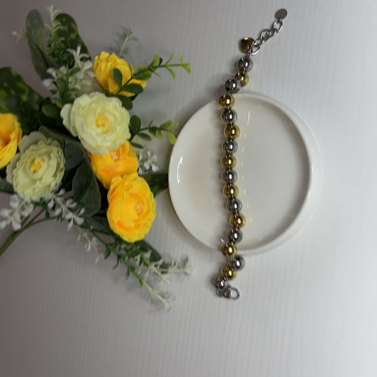 Elegante braccialetto con sfere dorate e argentate lucide su fiori gialli e foglie verdi
