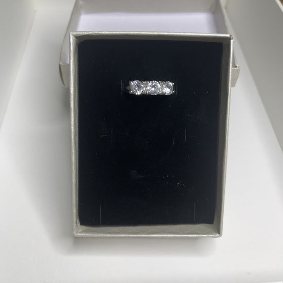Anello Trio in acciaio premium placcato argento con tre zirconi brillanti perfettamente incastonati, fotografato su superficie scura che esalta la brillantezza delle pietre