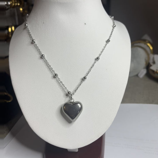  Collana Allegra in acciaio premium con catena decorata da sfere e ciondolo cuore, variante placcato argento, esposta su busto espositore bianco 