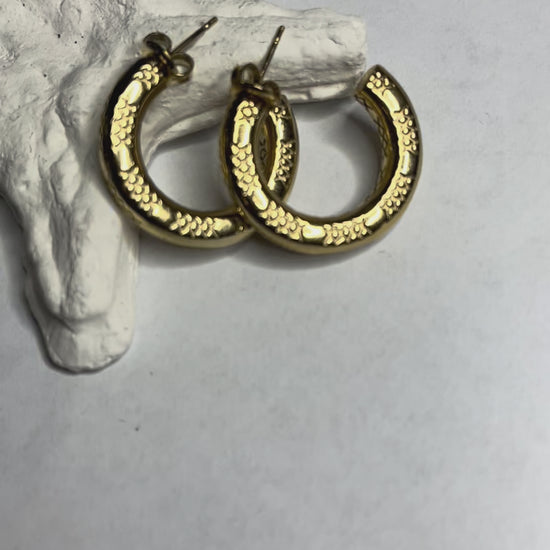 Orecchini a cerchio placcati oro con texture decorativa tridimensionale, appoggiati su corallo bianco