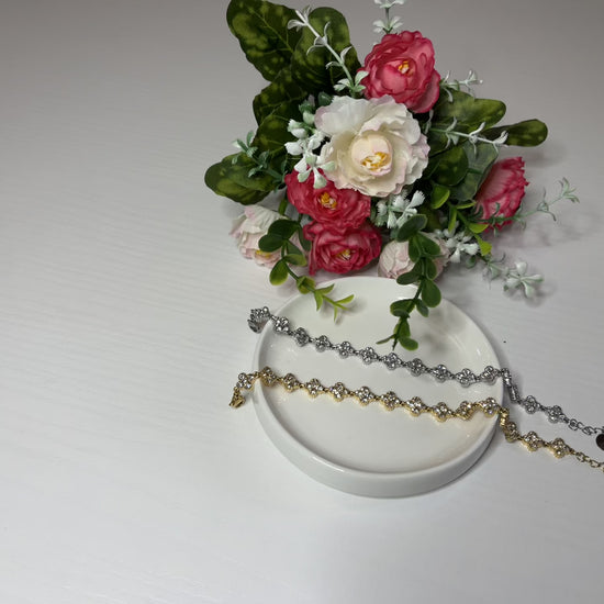  Braccialetti tennis, uno placcato oro, uno placcato argento con quadrifogli portafortuna e cristalli scintillanti su sfondo bianco con foglie verdi