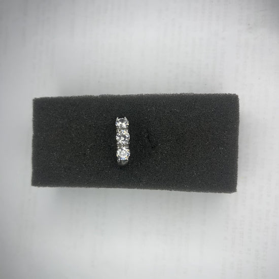 Anello Trio in acciaio premium placcato argento con tre zirconi brillanti perfettamente incastonati, fotografato su superficie scura che esalta la brillantezza delle pietre