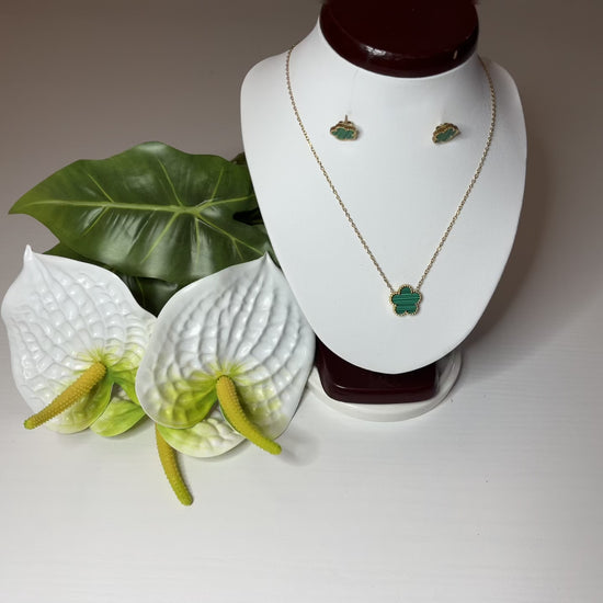 Set Elegance con collana e orecchini coordinati con pietre verdi smeraldo su catena dorata, esposto su busto bianco con decorazioni floreali