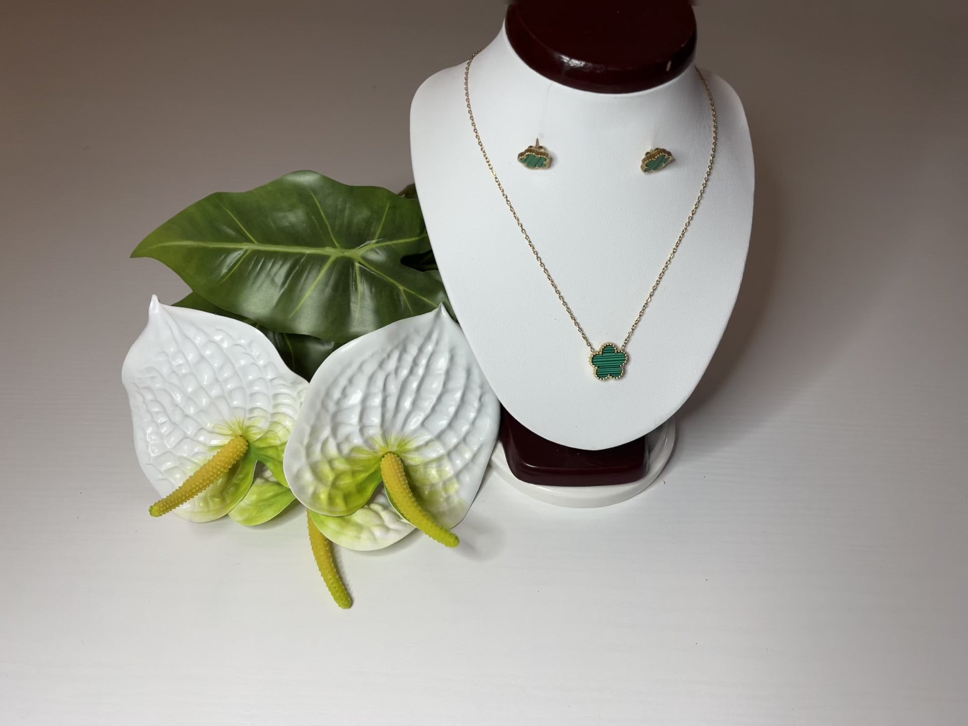 Set Elegance con collana e orecchini coordinati con pietre verdi smeraldo su catena dorata, esposto su busto bianco con decorazioni floreali