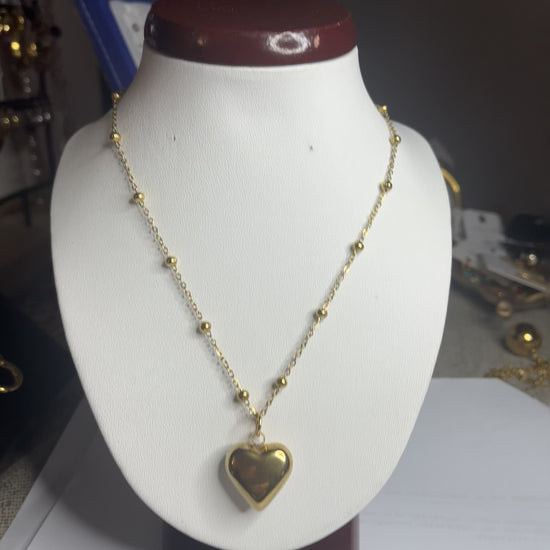  Collana Allegra in acciaio premium con catena decorata da sfere e ciondolo cuore, variante placcato oro, esposta su busto espositore bianco 