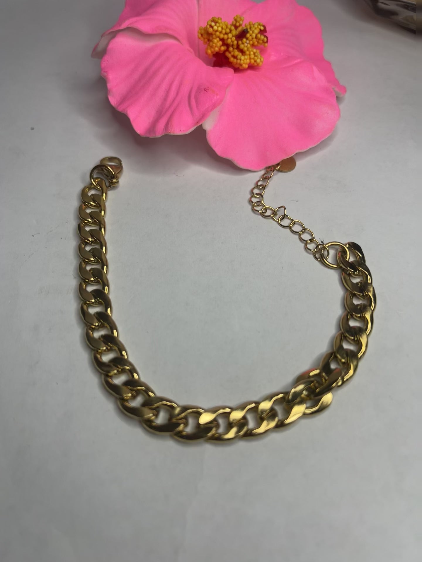 Bracciale Bold Chain placcato oro con maglie chunky grandi su sfondo grigio con petali rosa