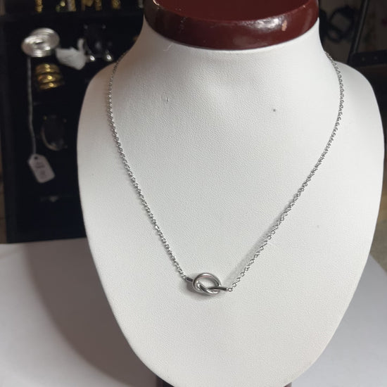 Collana Love Knot con pendente a nodo intrecciato dorato su catena delicata, simbolo di amore eterno esposto su busto bianco
