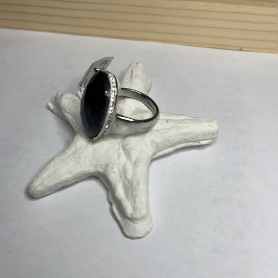  Anello con pietra nera ovale lucida e montatura argentata o dorata decorata, appoggiato su stella marina bianca